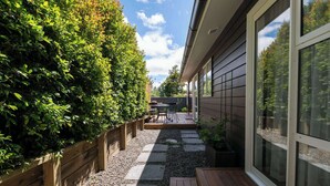 A patio with a table and chairs, a wooden fence, and a gravel path leading to a house with large windows. - Inn McDowell - Modern 3-Bed, Minutes to Te Puia (Rotorua)