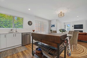 A modern kitchen with white cabinets, a stainless steel dishwasher, and a wooden dining table. - Inn McDowell - Modern 3-Bed, Minutes to Te Puia (Rotorua)