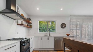 A modern kitchen with white cabinets, a gas stove, a dishwasher, and a window with blinds. - Inn McDowell - Modern 3-Bed, Minutes to Te Puia (Rotorua)
