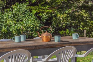 A wooden table with a copper teapot and two matching cups, surrounded by white chairs.