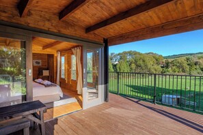 Una cabaña de madera con balcón, una cama con toallas y vistas a un paisaje verde.