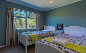 A bedroom with two beds, a window with curtains, a bedside table, and a wall with a sign.
