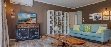 Una sala de estar con una mesa de centro de madera, un sofá azul, una estantería blanca y un televisor que muestra una imagen panorámica.