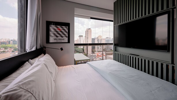 A modern hotel room with a large bed, a mounted TV, and a city view. - DAWN 145 (Vila Olímpia São Paulo)
