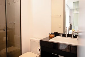 A modern bathroom with a glass shower enclosure, a toilet, and a sink with a black countertop.