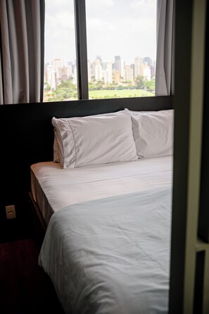 A hotel room with a bed, curtains, and a view of a cityscape through large windows.