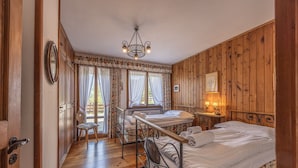 Un dormitorio con paneles de madera, dos camas, una silla, una mesita con lámpara y un candelabro.