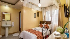 Habitación de hotel con cama, mesita de noche, lámpara y un pequeño escritorio con teléfono y un florero.
