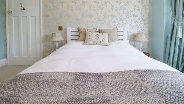 A bedroom with a bed, two bedside lamps, a door, and floral wallpaper. - Hathaway Lane (Stratford-upon-Avon)