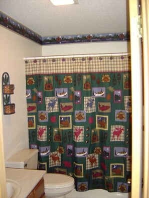 A bathroom with a green shower curtain featuring animal prints, a white toilet, and a wooden cabinet.