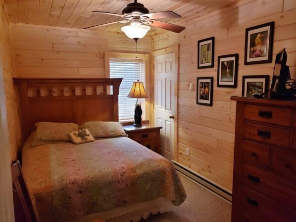 A wooden cabin bedroom with a bed, nightstands, a dresser, and a ceiling fan.