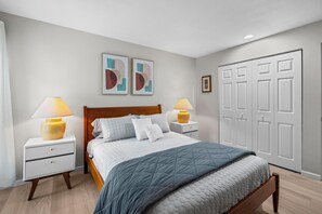 Ein Schlafzimmer mit einem hölzernen Bett, zwei Nachttischen mit Lampen, einem weißen Kleiderschrank und zwei abstrakten Bildern an der Wand.