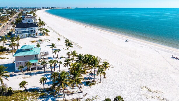 A beachfront property with a large house, a sandy beach, and palm trees.