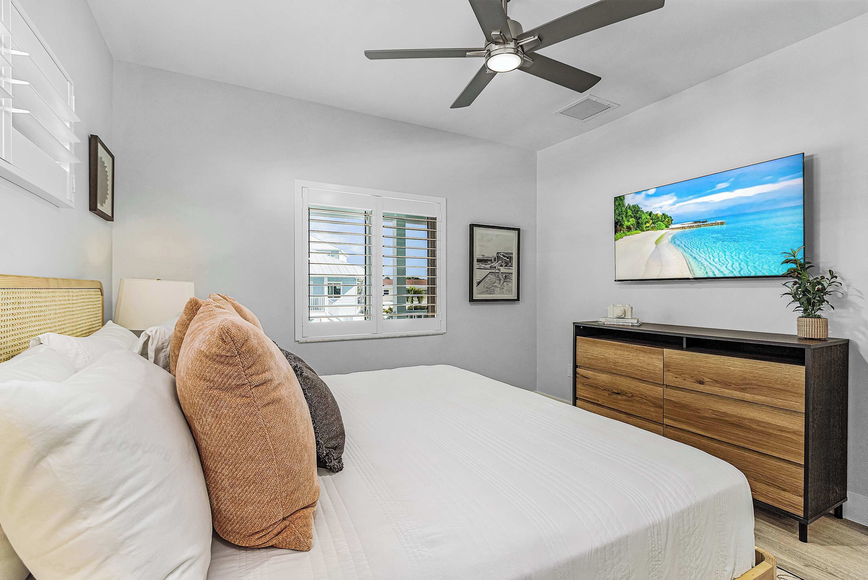 A bedroom with a bed, a ceiling fan, a TV, a window with blinds, a bedside table, and a dresser.