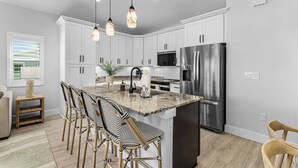 A modern kitchen with white cabinets, a central island with bar stools, stainless steel appliances, and pendant lighting.