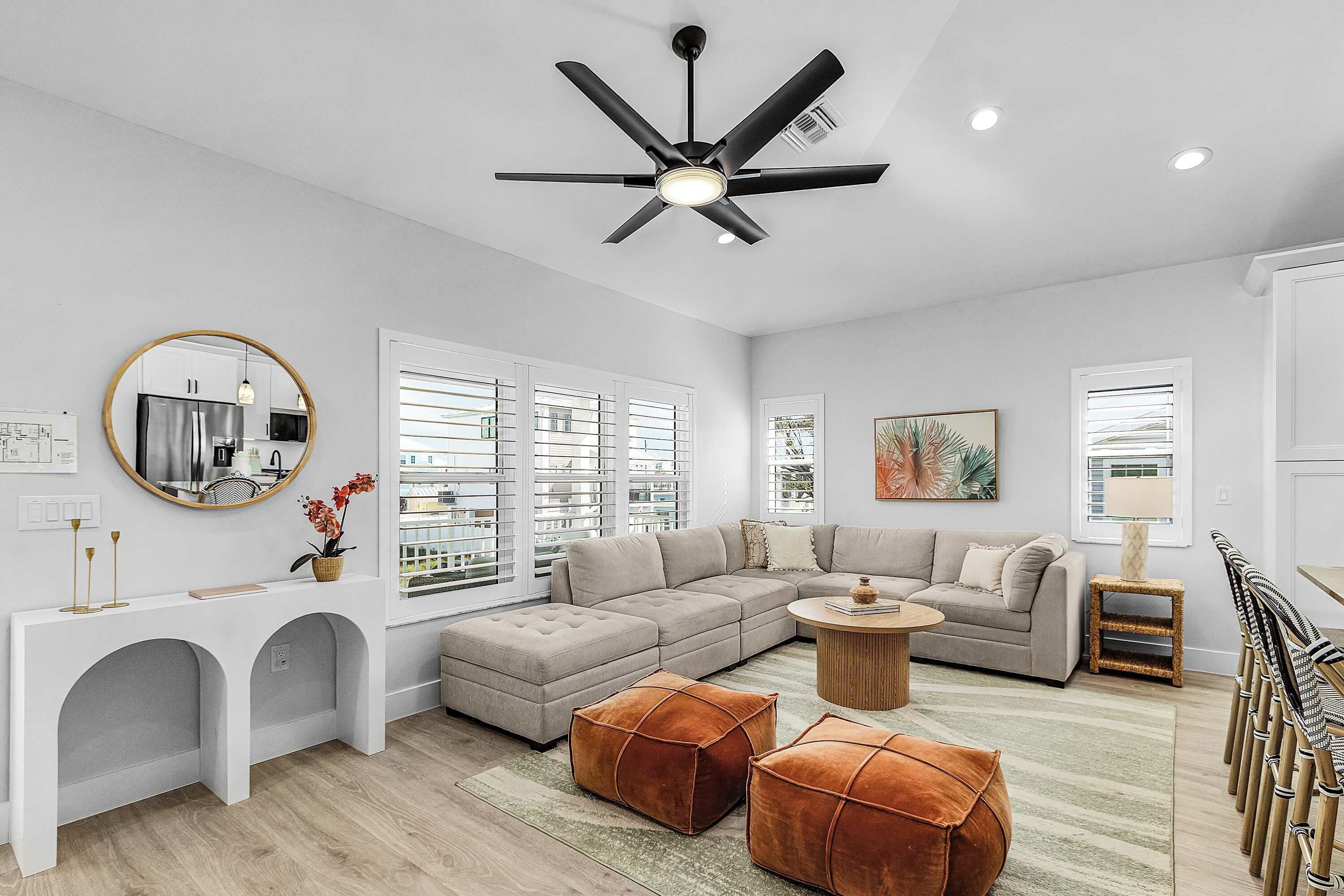 A modern living room with a sectional sofa, ottomans, a coffee table, and a ceiling fan.