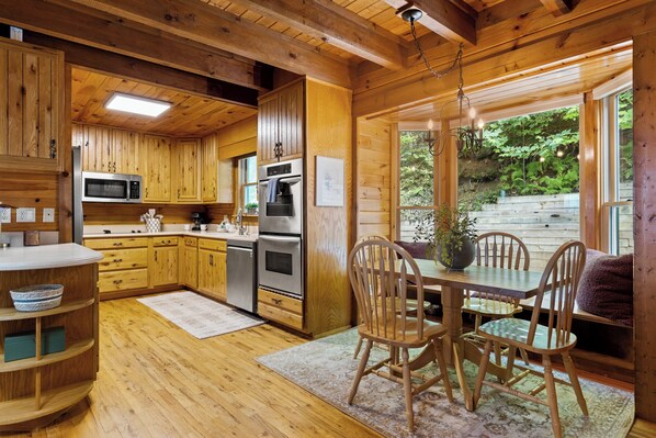 Une cuisine en bois, aménagée avec des appareils intégrés, une table à manger avec des chaises et une vue sur la forêt environnante.