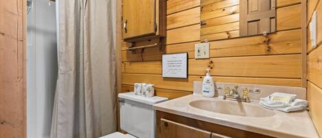 Bagno con rivestimento in legno, dotato di WC, lavandino e tenda per la doccia.