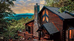 A log cabin with a stone chimney, wooden deck, and a scenic mountain view. - Heinrich's Hideaway Blue Ridge, GA (MORGANTON)