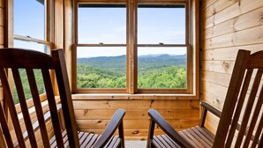 A wooden cabin room with two large windows offering a view of a forested mountain range. - Heinrich's Hideaway Blue Ridge, GA (MORGANTON)