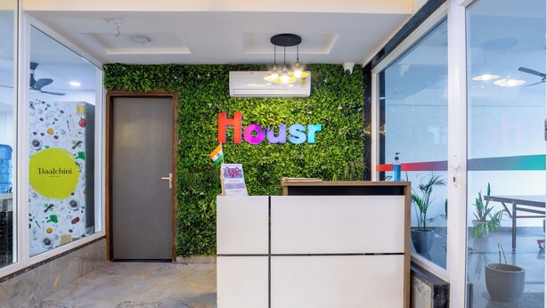 A reception area with a green wall, a sign reading "Housr", and a ceiling fan. - Housr Sector 43 Gurgaon Global FoyerMall (Gurugram)
