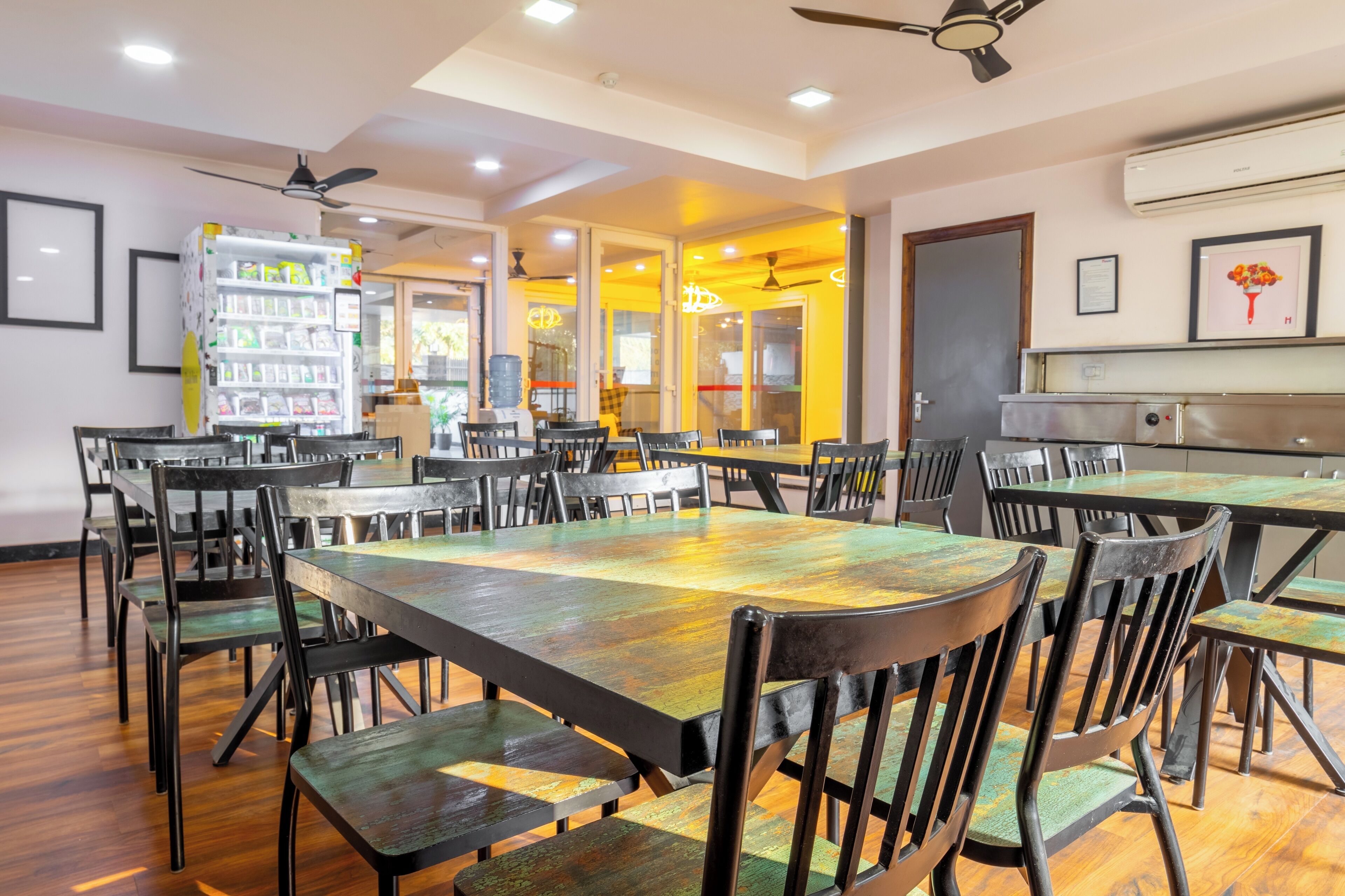 A dining area with multiple tables and chairs, a refrigerator, and ceiling fans.
