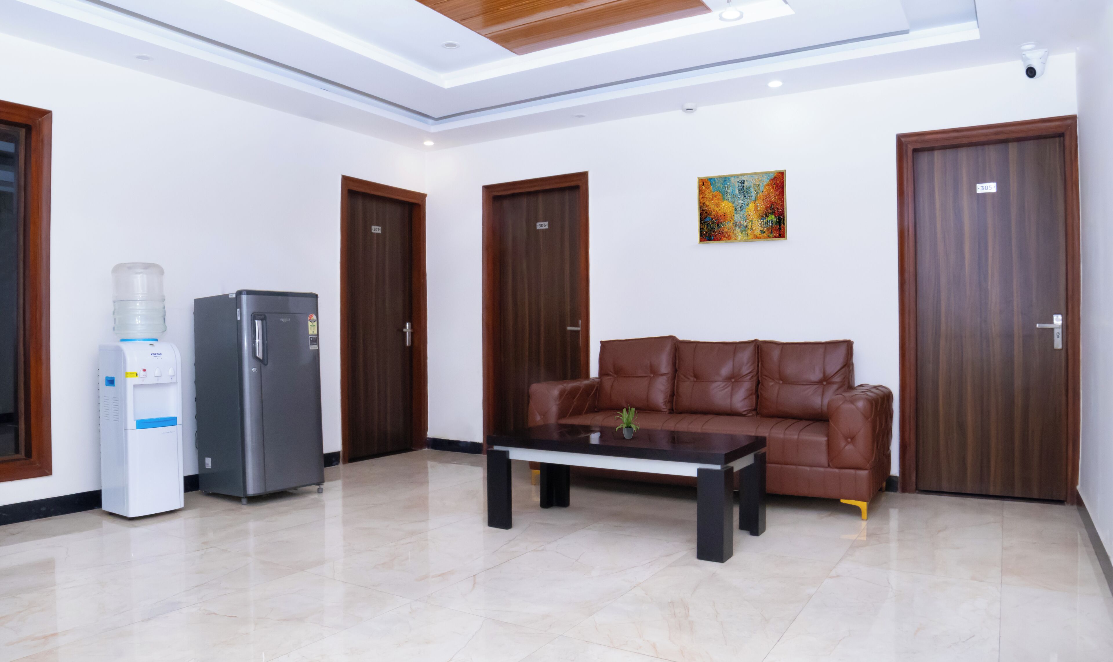 A modern living room with a brown leather sofa, a coffee table, a water dispenser, and a refrigerator.