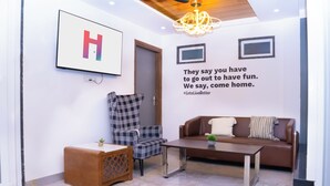 A modern living room with a large H framed picture, a plaid chair, a brown sofa, and a coffee table. - Housr Sector 43 Gurgaon Global FoyerMall (Gurugram)