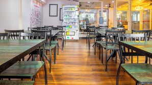 A restaurant with wooden tables and chairs, a whiteboard with drawings, and a shelf with food items. - Housr Sector 43 Gurgaon Global FoyerMall (Gurugram)