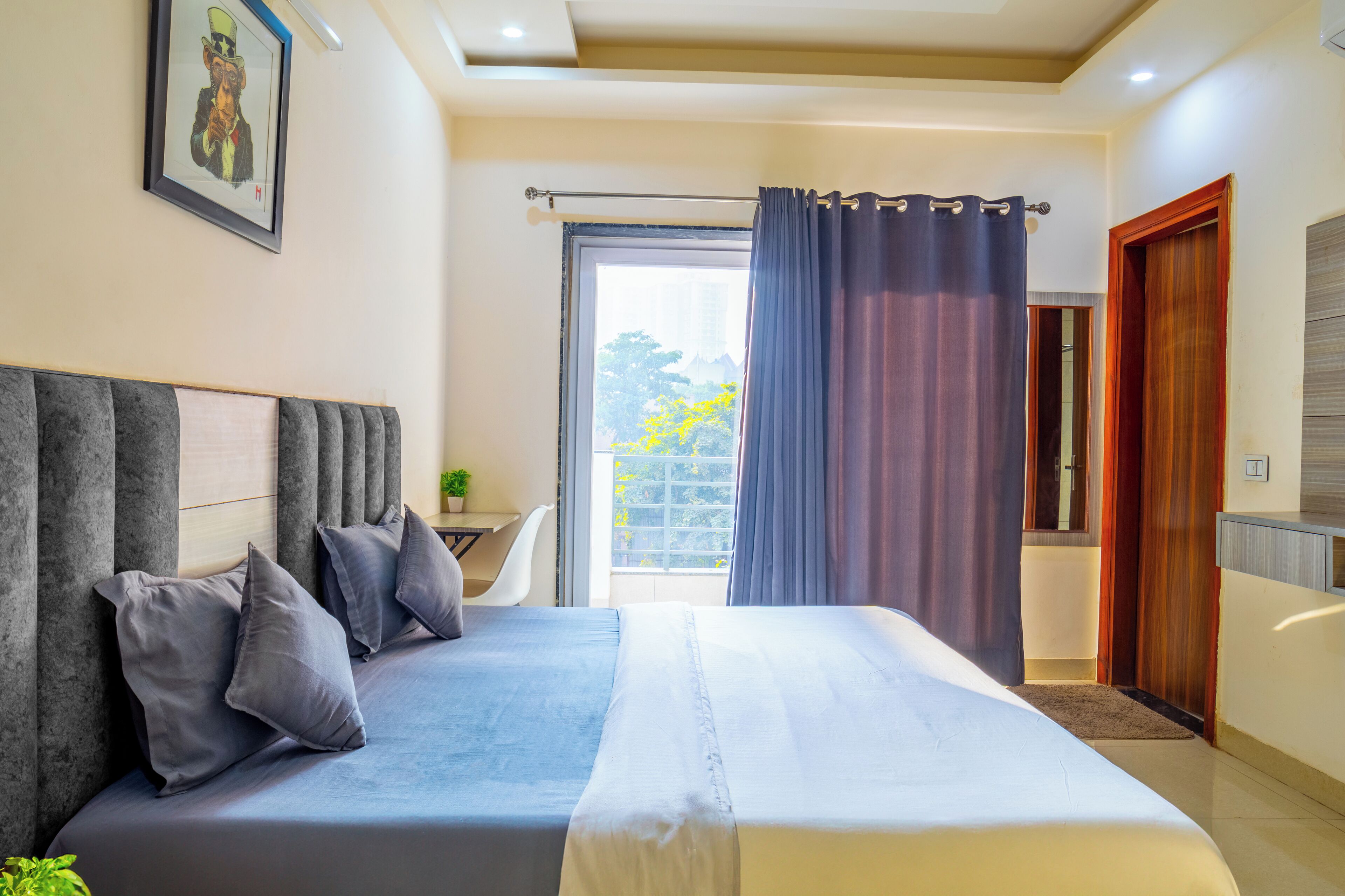 A modern bedroom with a large bed, a desk, and a view of the outdoors.