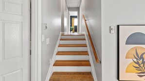 A hallway with white walls, a wooden staircase, and a framed artwork on the wall.