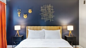 A bedroom with a dark blue wall, a geometric light fixture, and two bedside tables with lamps.