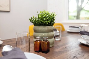Une table à manger ornée d’une plante verte dans un pot en céramique, de deux petits flacons en verre et d’un verre d’eau.