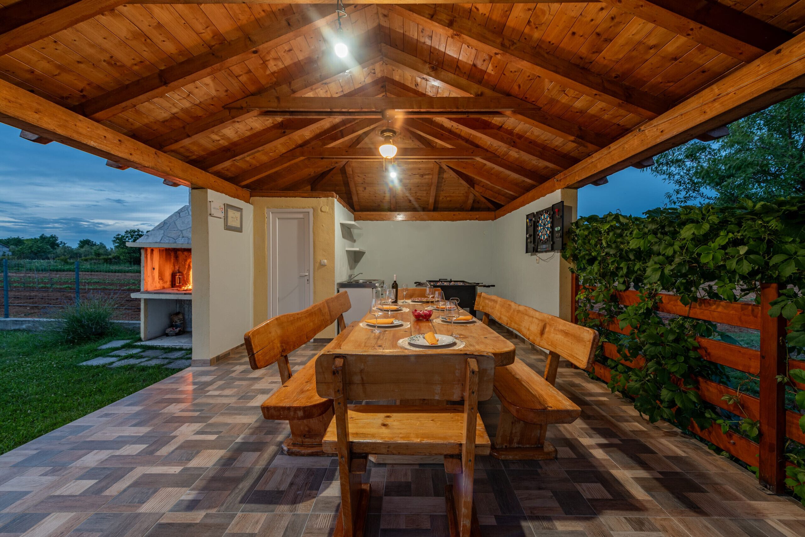 Un espacio exterior para comer con una mesa y bancos de madera, rodeado de una valla de madera y un jardín.