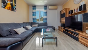 A modern living room with a sectional sofa, a glass coffee table, a flat-screen TV, wooden entertainment unit, and a large wall clock. - Villa Sami Zadar Villas (Benkovac)