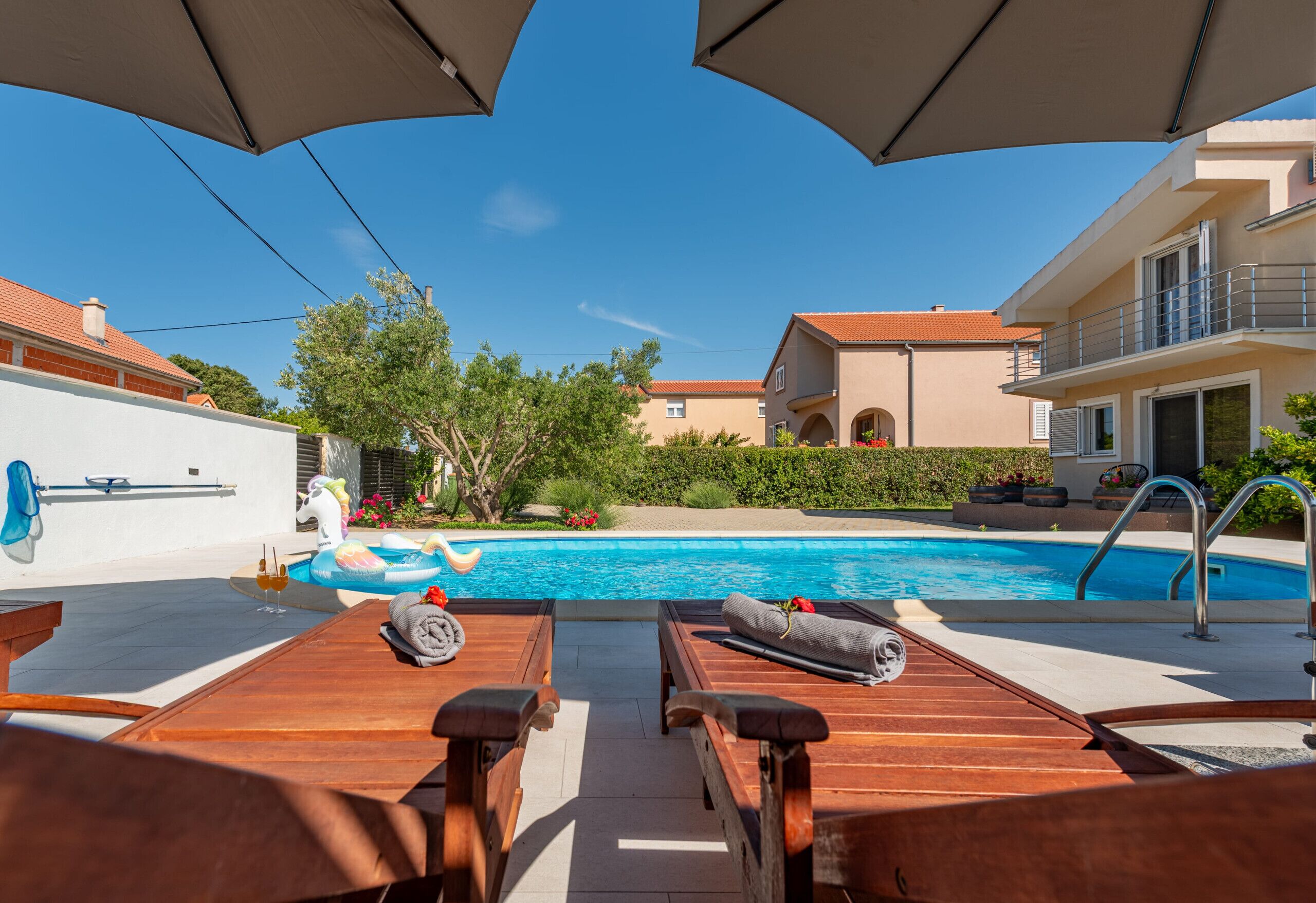 A poolside area with wooden lounge chairs, a pool, and umbrellas.