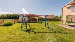 A grassy backyard with a swing set, a covered seating area, and a house in the background. - Villa Sami Zadar Villas (Benkovac)