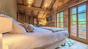 A wooden cabin bedroom with a bed, a TV, and large windows.