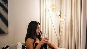 Une personne est assise sur un canapé gris, avec une bouteille et un verre posés sur une petite table à côté d’elle.