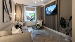 Un salon moderne avec un canapé, une table basse, un téléviseur fixé au mur et une fenêtre avec des rideaux.