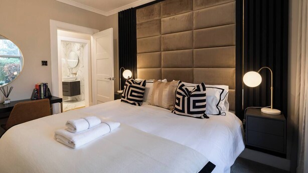 Une chambre d’hôtel avec un grand lit, une table de chevet avec une lampe, un bureau avec une chaise et une vue sur la salle de bain.