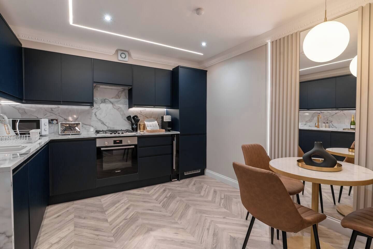 A modern kitchen with dark cabinetry, a marble backsplash, and a herringbone-patterned floor.