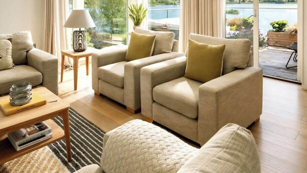 A spacious living room with a large window overlooking a lake, a modern chandelier, and a cozy seating area.