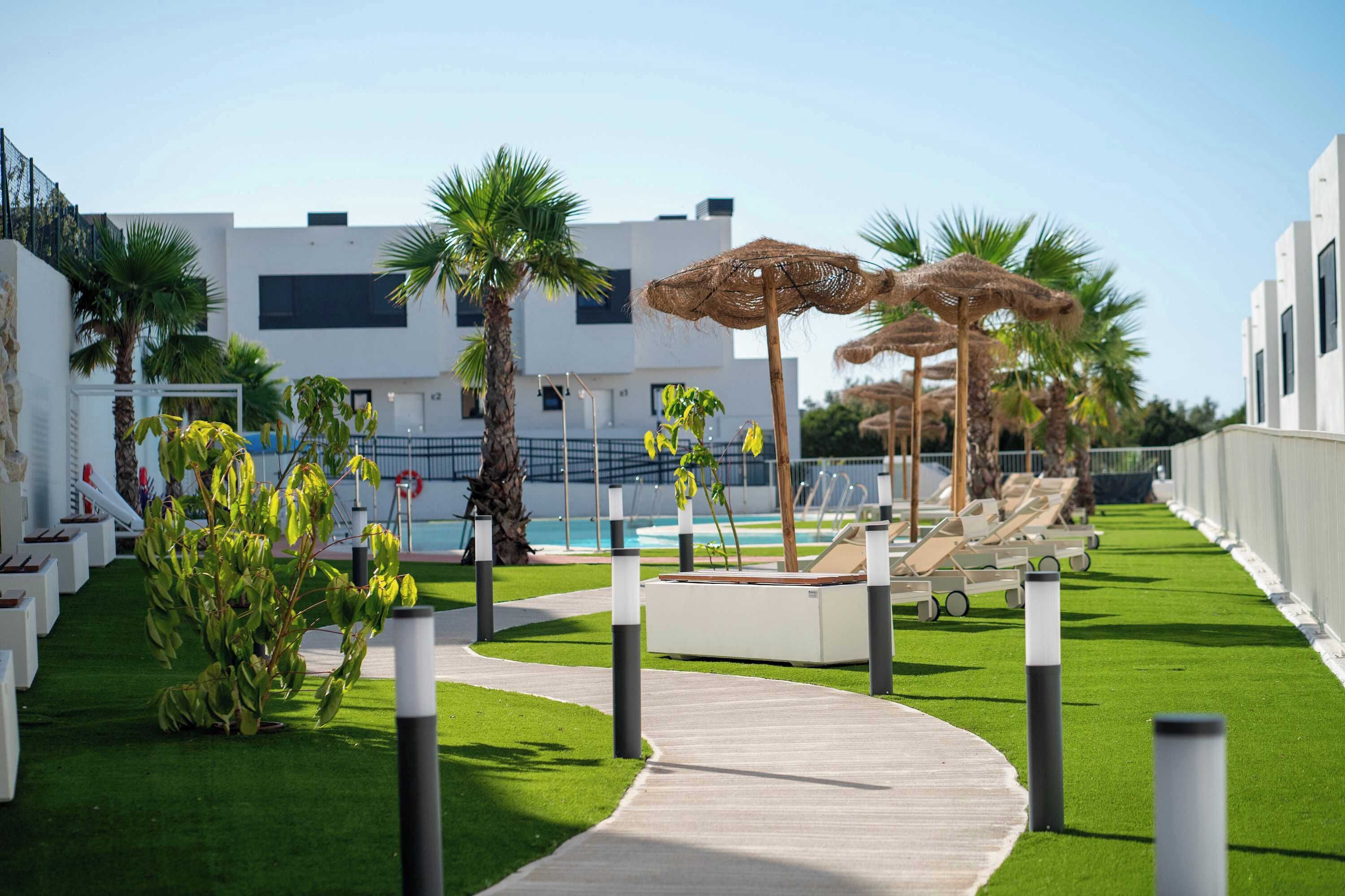 A poolside area with a pathway, lounge chairs, and umbrellas.