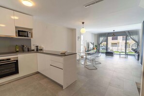 A modern kitchen with white cabinetry, a built-in microwave, and a dining area with a glass table and chairs.