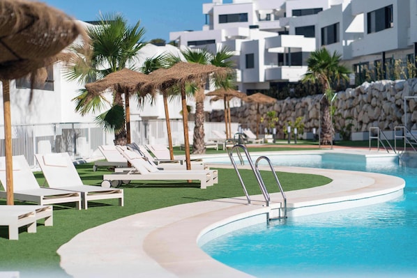 Un espace piscine agrémenté de chaises longues blanches, de palmiers et de parasols en chaume.
