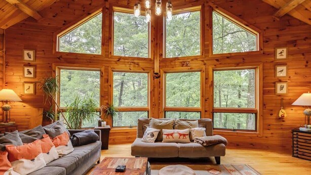 Interior acogedor de una cabaña con un techo grande de madera, un sofá, una mesa de centro y una mesa de comedor.