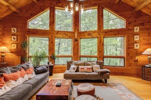 A cozy cabin interior with a large wooden ceiling, a sofa, a coffee table, and a dining table. - Wingspan Cabin (Keedysville)