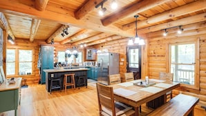 Interior de una cabaña de madera con cocina, comedor y ventanas amplias.