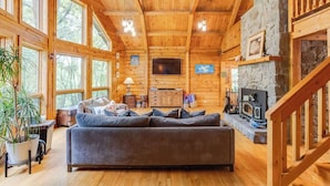 Interior acogedor de una cabaña con un sofá de madera grande, chimenea de piedra y una televisión.